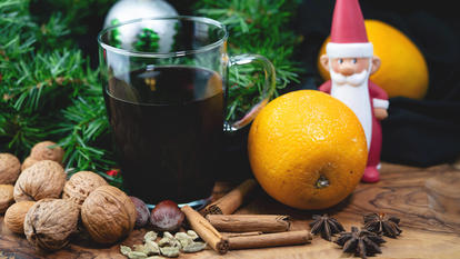 Eine Tasse Glühwein mit Orangen, Nüssen, Zimtstangen, und ein Weihnachtsmann als Deko