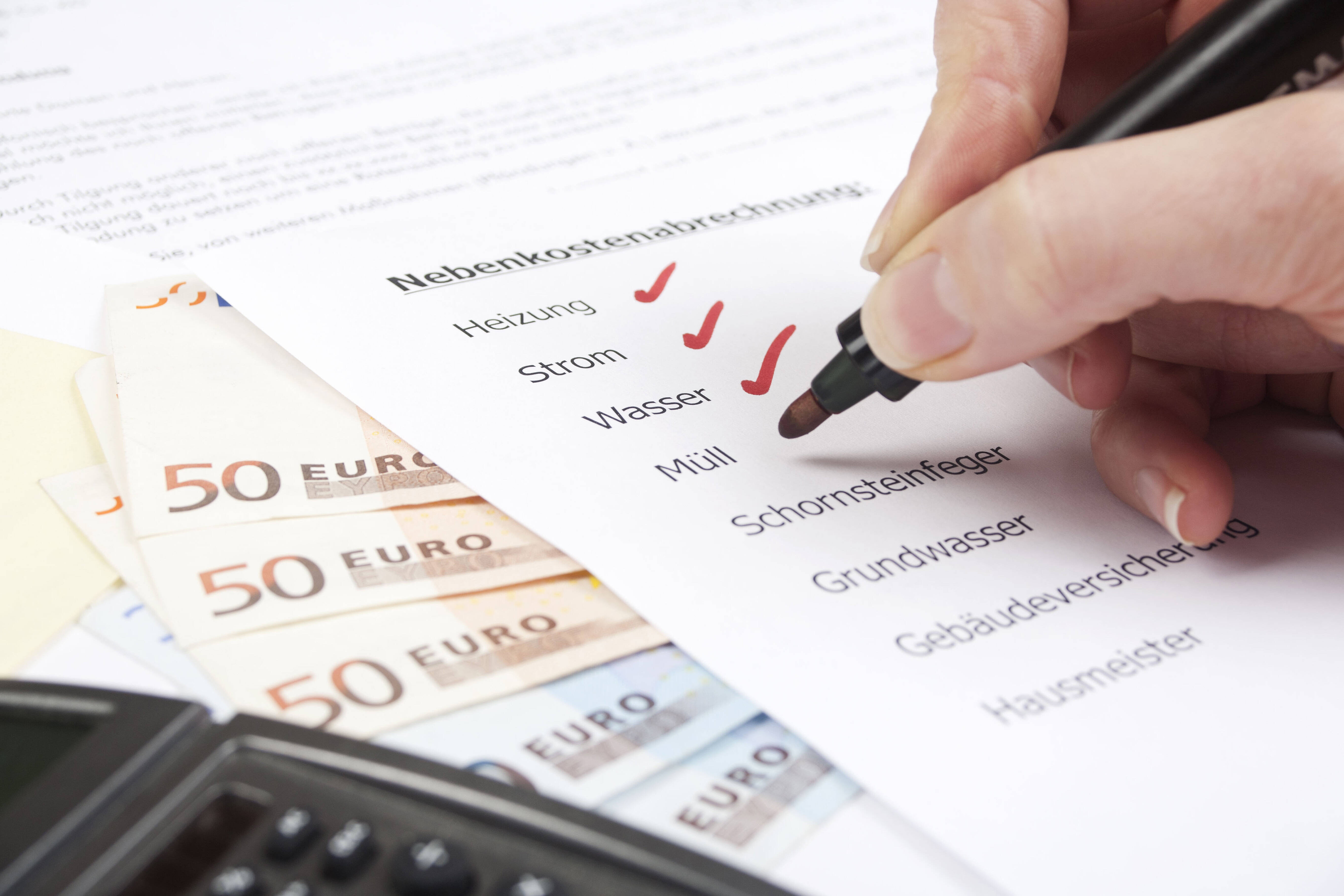 Ein Mann hakt die einzelnen Posten seiner Nebenkostenabrechnung ab. Daneben liegen Euro-Scheine und ein Taschenrechner.