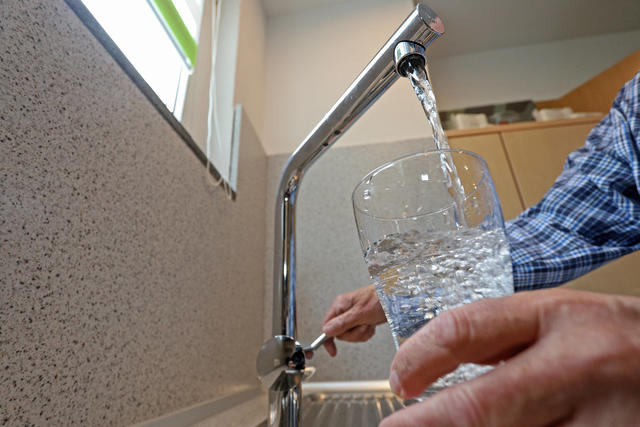 Ein Mann befüllt ein Glas mit Leitungswasser aus dem Wasserhahn