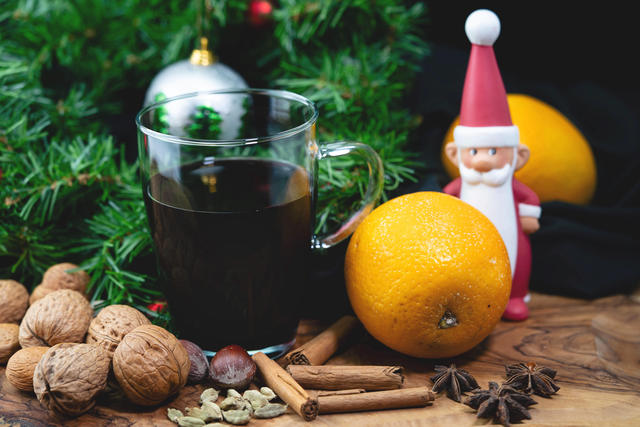 Eine Tasse Glühwein mit Orangen, Nüssen, Zimtstangen, und ein Weihnachtsmann als Deko