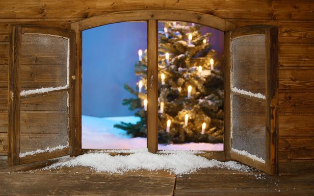 Ein Fenster steht offen und gibt den Blick auf einen beleuchteten Weihnachtsbaum und eine Schneelandschaft frei.