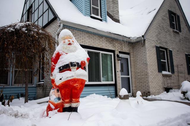 Ein Weihnachtsmann steht in einem schneebedeckten Garten vor einem Haus