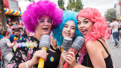 Drei bunt verkleidete junge Frauen singen in drei aufblasbare Mikrofone