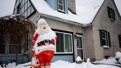 Ein Weihnachtsmann steht in einem schneebedeckten Garten vor einem Haus