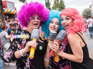 Drei bunt verkleidete junge Frauen singen in drei aufblasbare Mikrofone