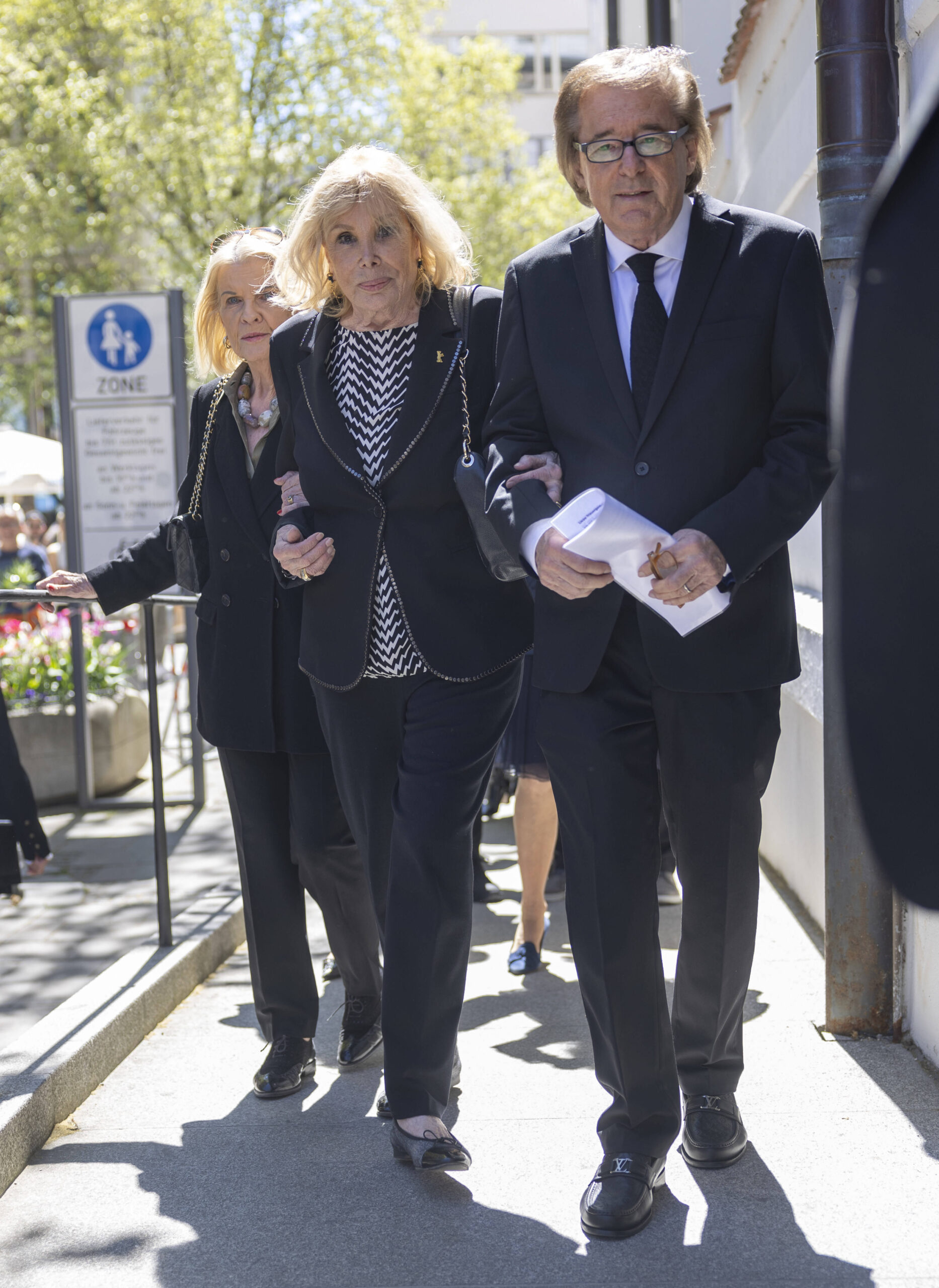 Mario Adorfs Witwe Monique Faye wird bei der Trauerfeier in München von Freunden gestützt