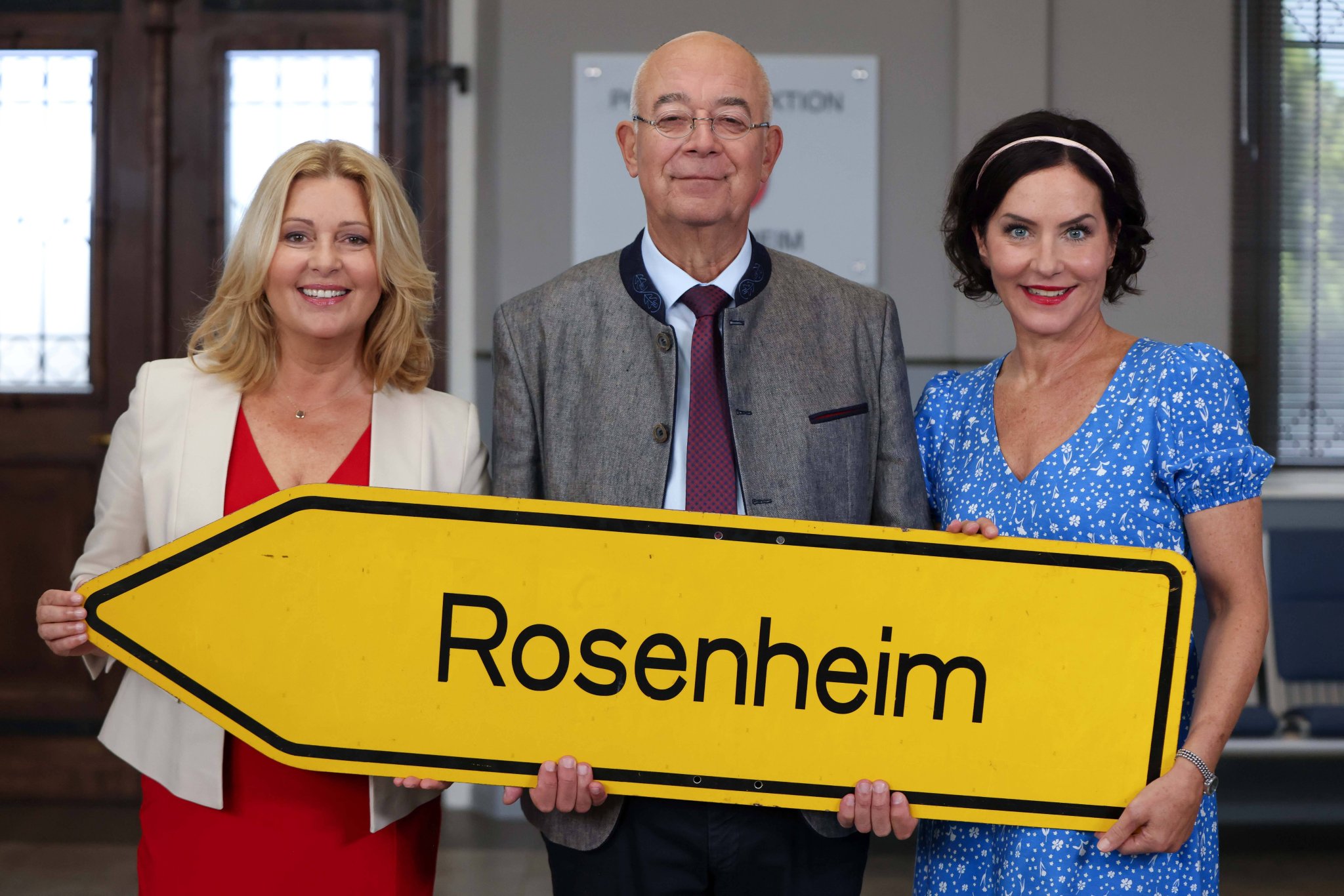 Karin Thaler, Alexander Duda und Marisa Burger halten ein Ortsschild „Rosenheim“ beim Fotocall der Rosenheim-Cops