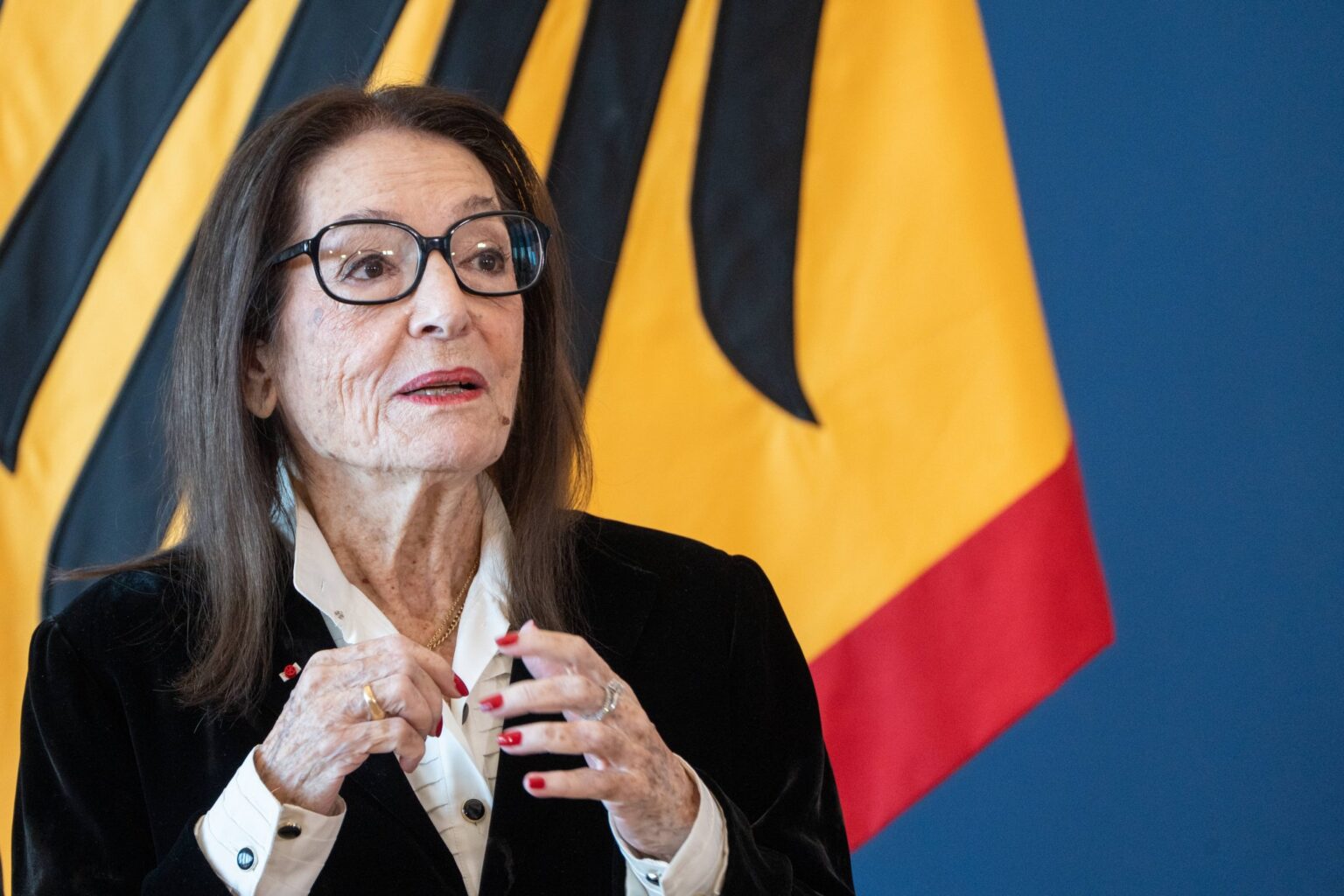 Nana Mouskouri spricht bei der Ordensverleihung des Bundespräsidenten in Berlin vor einer Deutschlandflagge